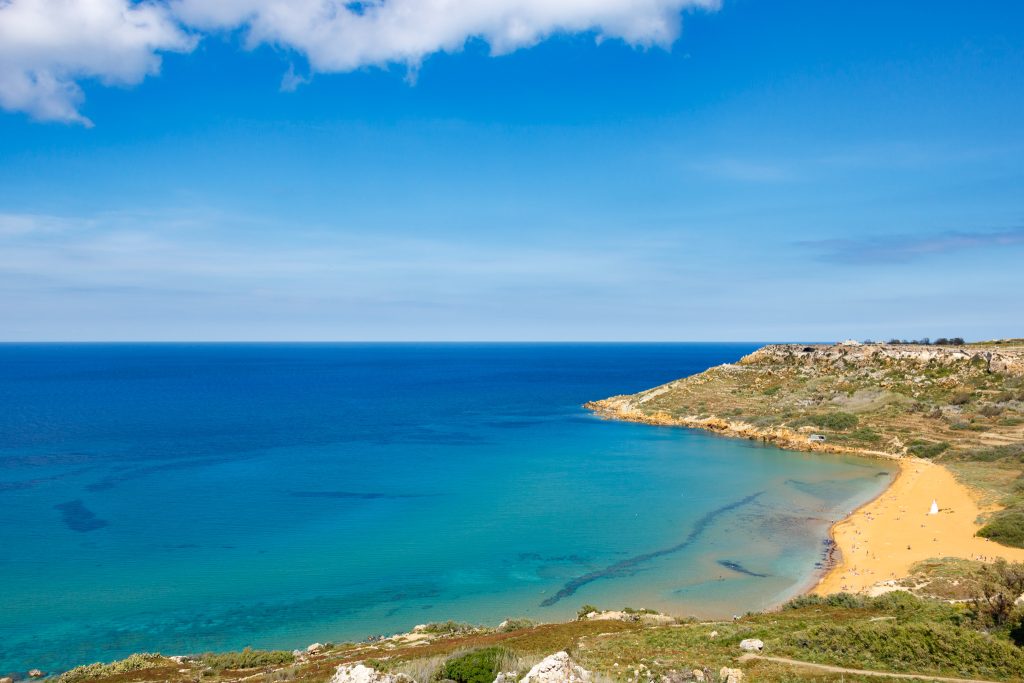 A bright orange crescent of sand leads to electric blue water at Ramla Bay on Gozo Island, Malta.