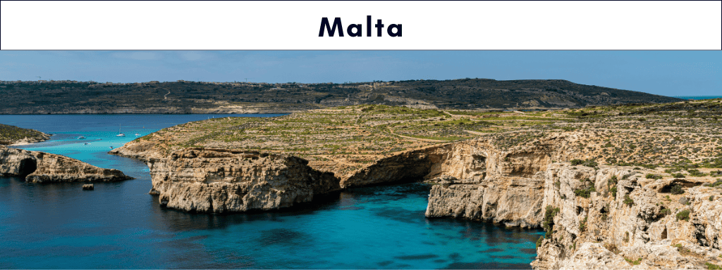 Golden limestone cliffs tower above bright blue sea in an aerial panorama of the Maltese coast