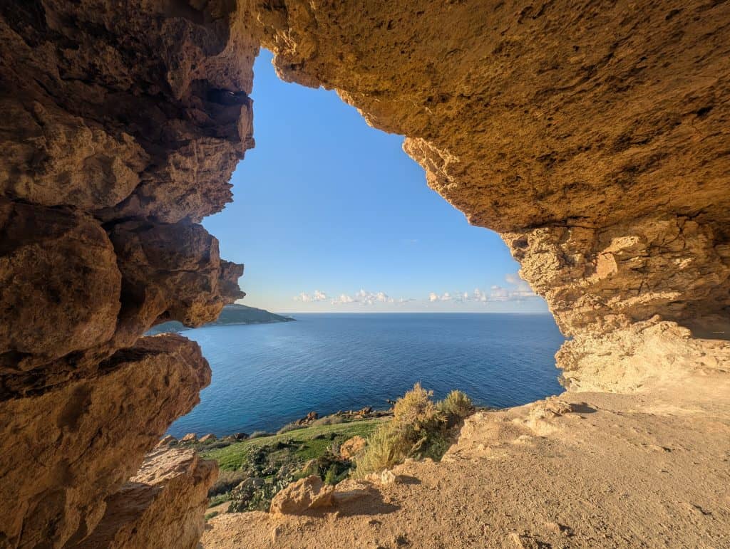 The glowing golden stone walls and roof of a Maltese cave frame a vast stretch of deep blue sea