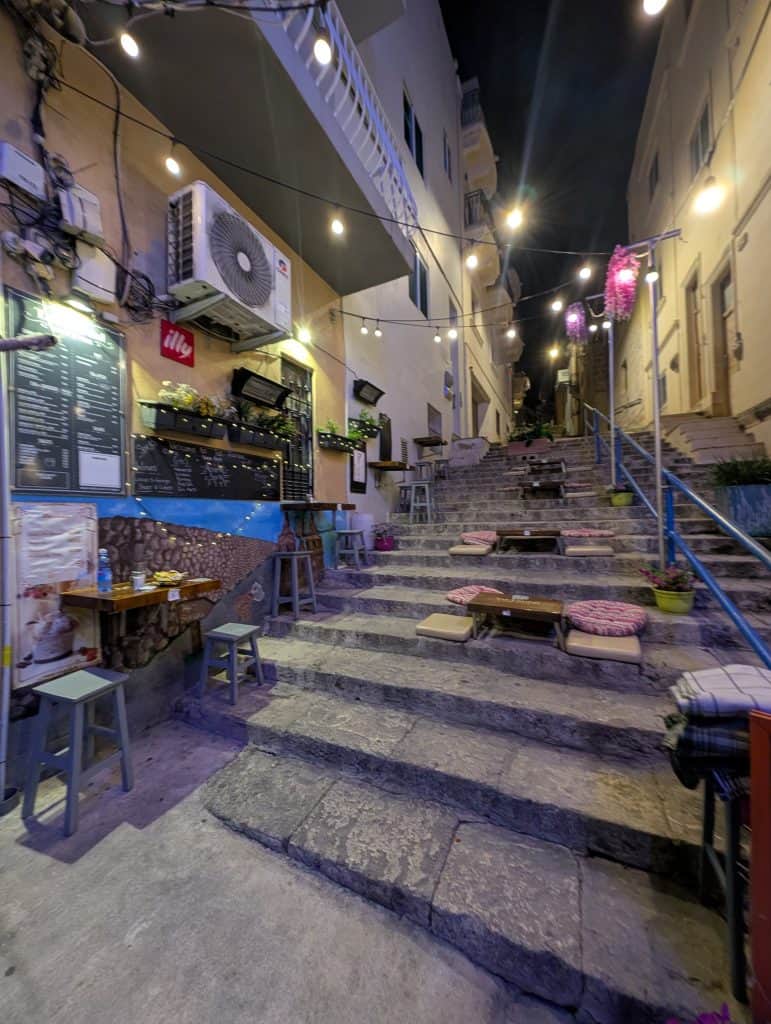 Stools, cushions, and blankets arrayed on the ancient stone steps near Tar-Fardal street food in Mellieha, Malta. 