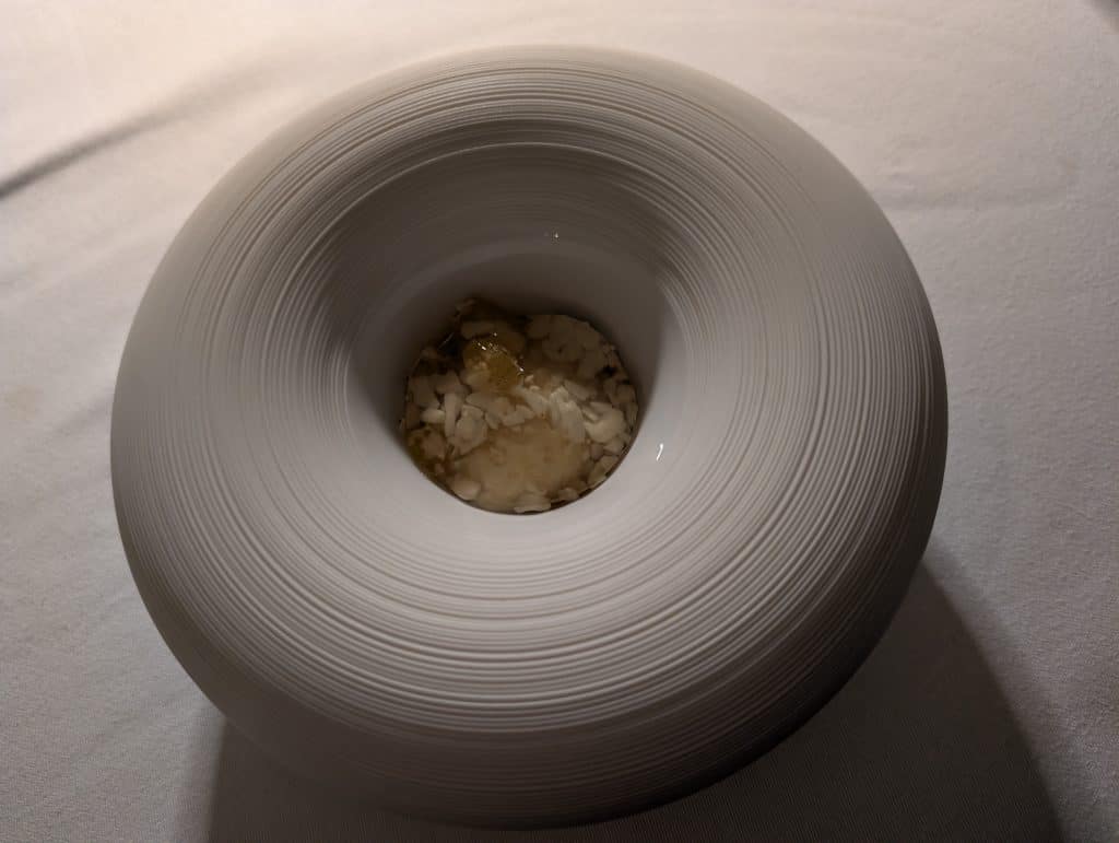 A small portion of white ice cream topped with small pieces of rock candy sits in the center of an artfully striated white bowl. 