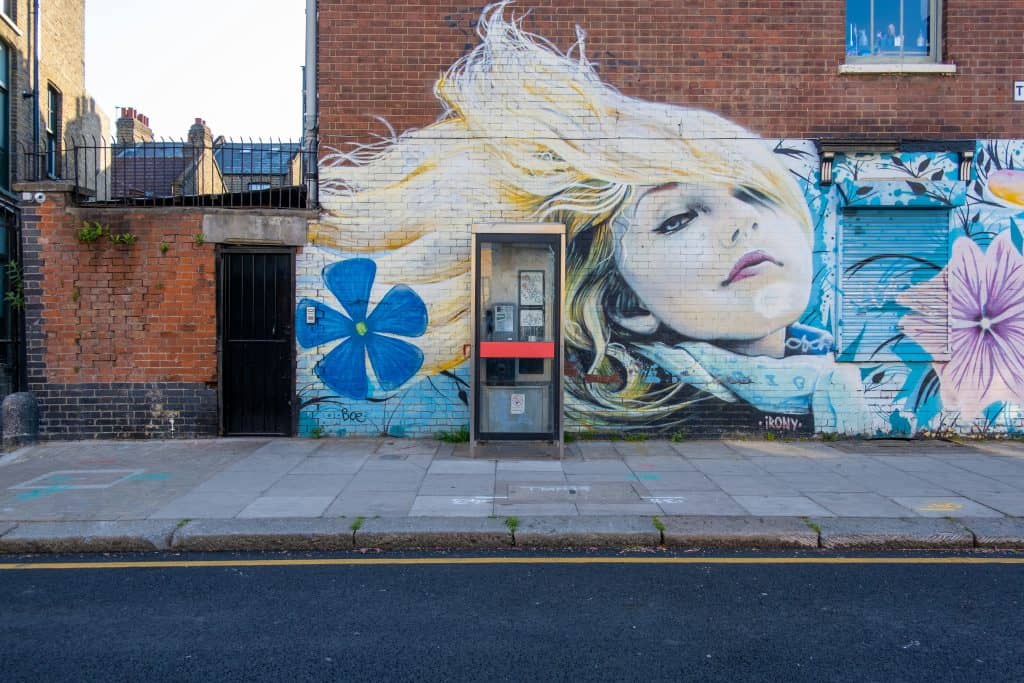 A street art mural of a young woman with long blonde hair blowing behind her on a brick building in Bethnal Green, London